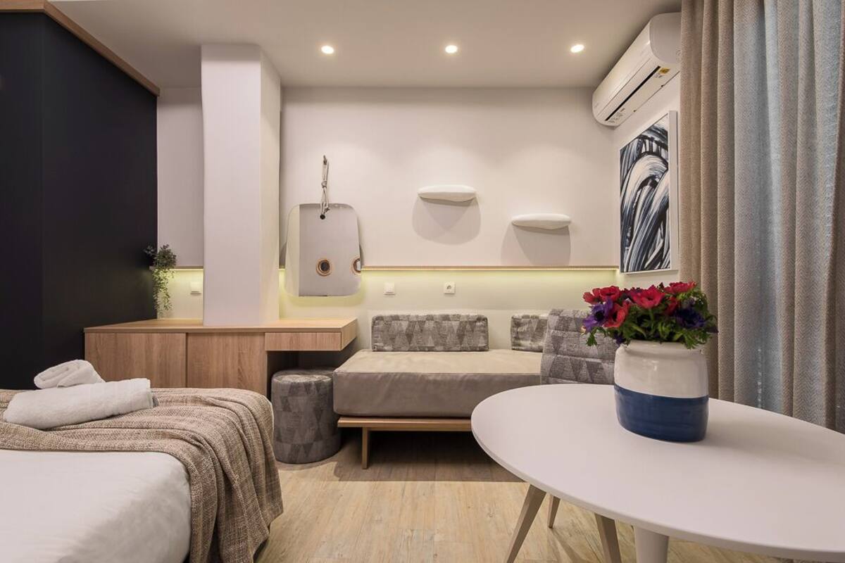 A modern hotel room with a bed, a sofa, a small table, and a decorative vase.