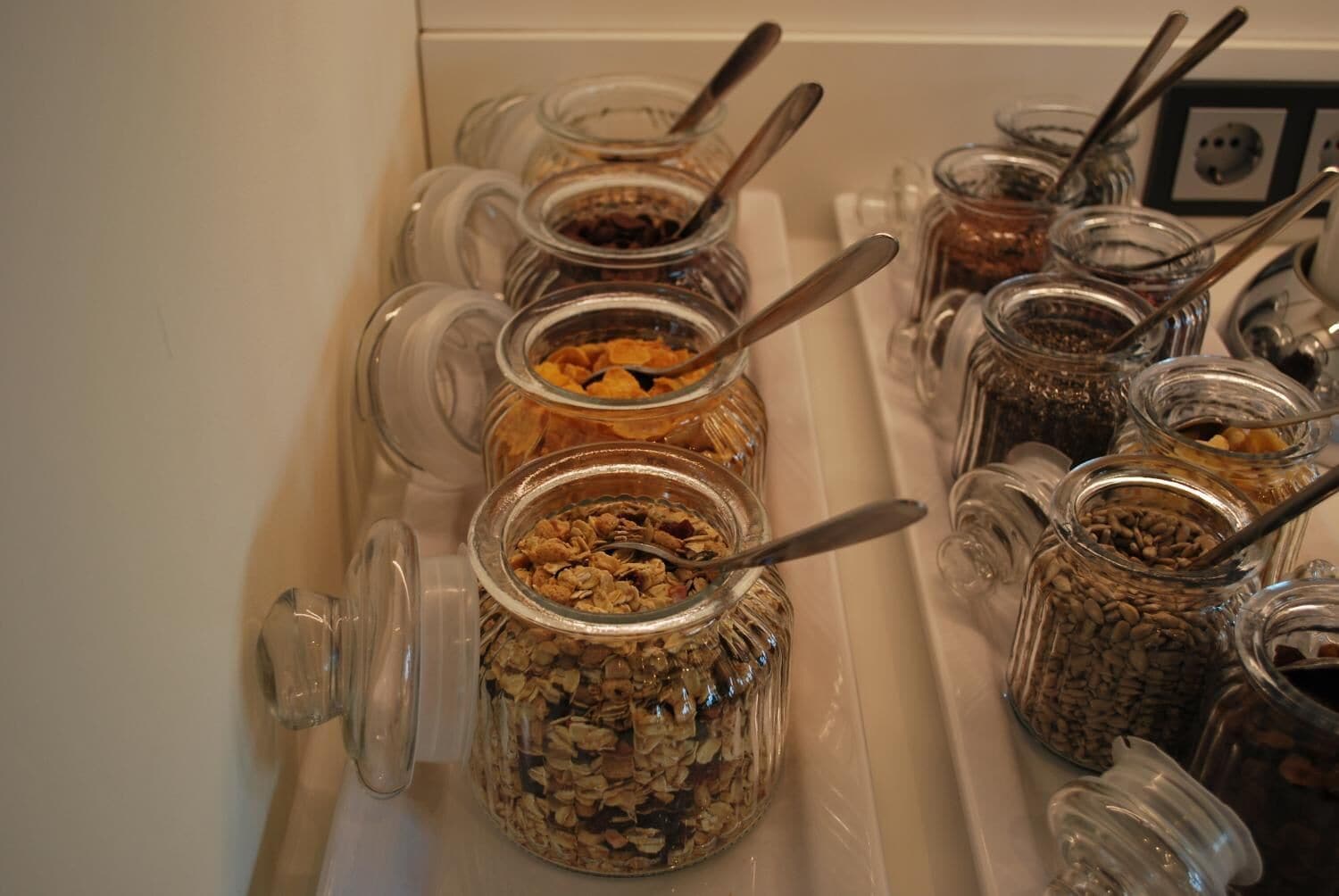 A food station with various jars containing different types of snacks and spreads, each with a spoon.