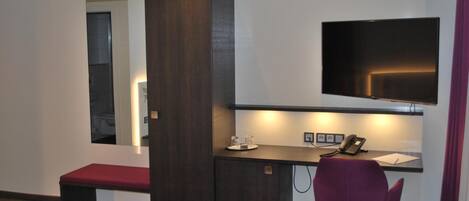 Una habitación pequeña y moderna con un escritorio, una silla y un televisor fijado a la pared.