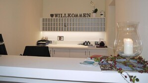 A modern reception area with a 'WILLKOMMEN' sign, a glass vase with a candle, and a decorative wreath. - Hotel am Berg Esslingen (Esslingen)