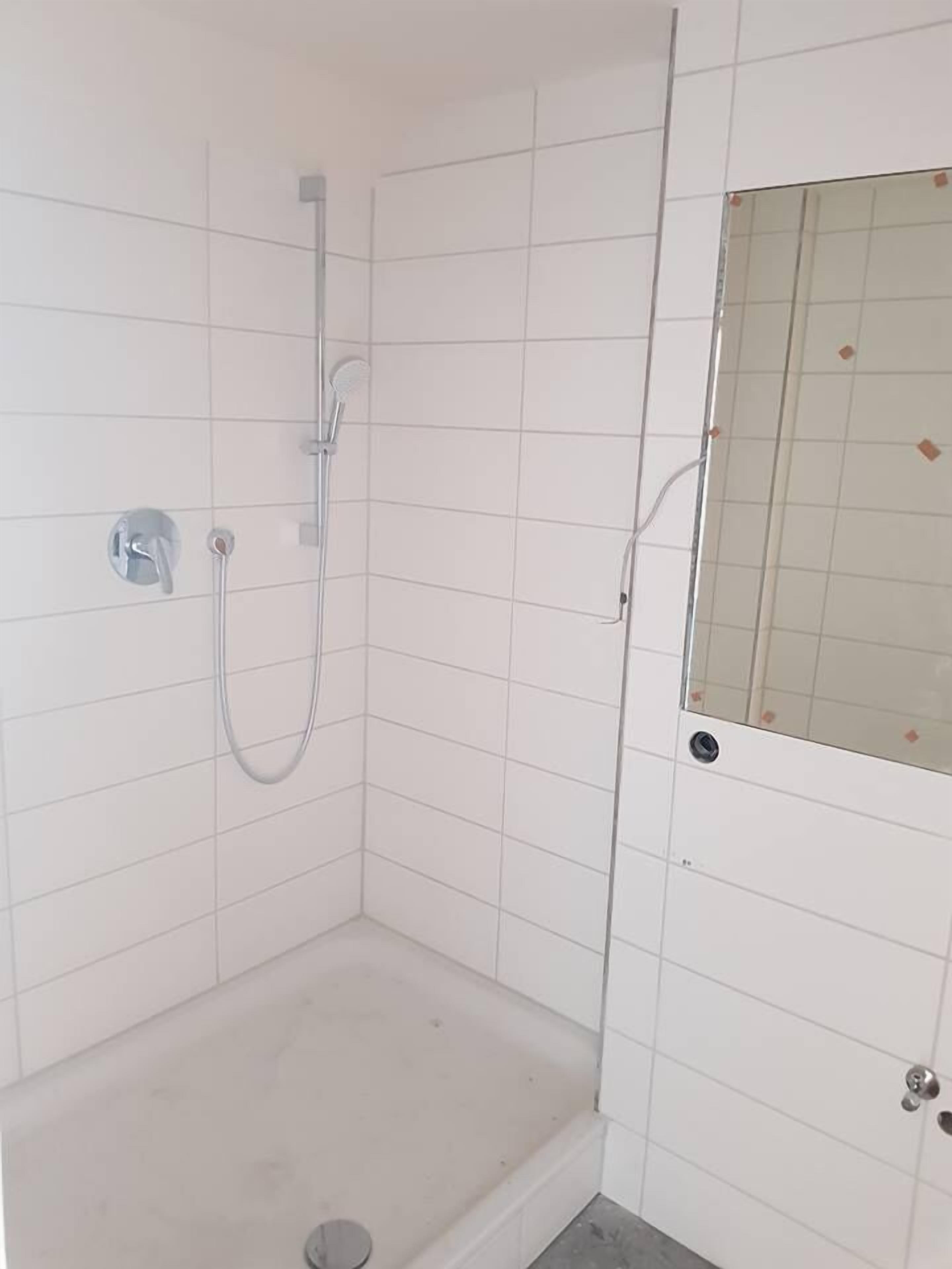 Un pequeño espacio de ducha con azulejos, un cabezal de ducha manual y un grifo instalado en la pared.