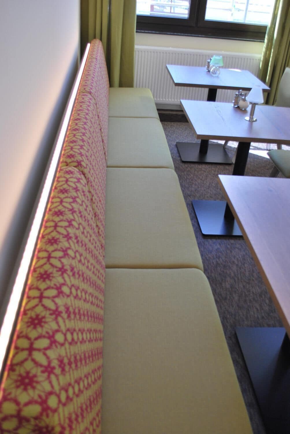 A seating area with a patterned bench, a table, and a window with curtains.