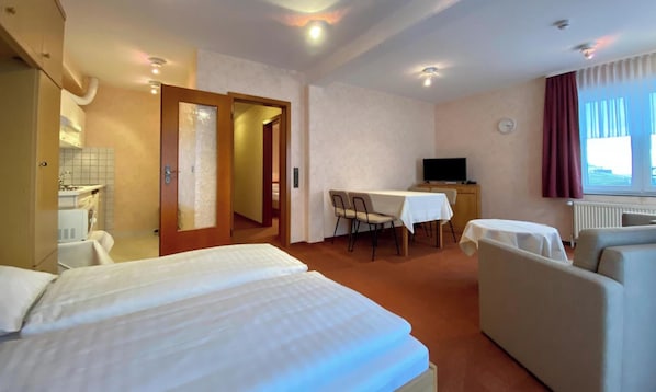 A hotel room with a bed, a desk with a chair, a sofa, and a television.