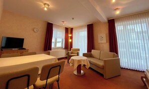 Una habitación de hotel con una mesa de comedor, dos sofás, un televisor y una mesita de noche con una lámpara.