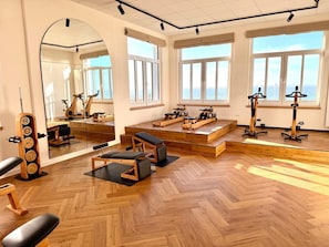 A spacious gym with wooden flooring, exercise equipment, and large windows offering views.