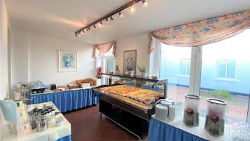 Ein reichhaltiges Buffet mit verschiedenen Speisen und Getränken, eine Kaffeestation und ein Fenster mit Blick nach draußen.