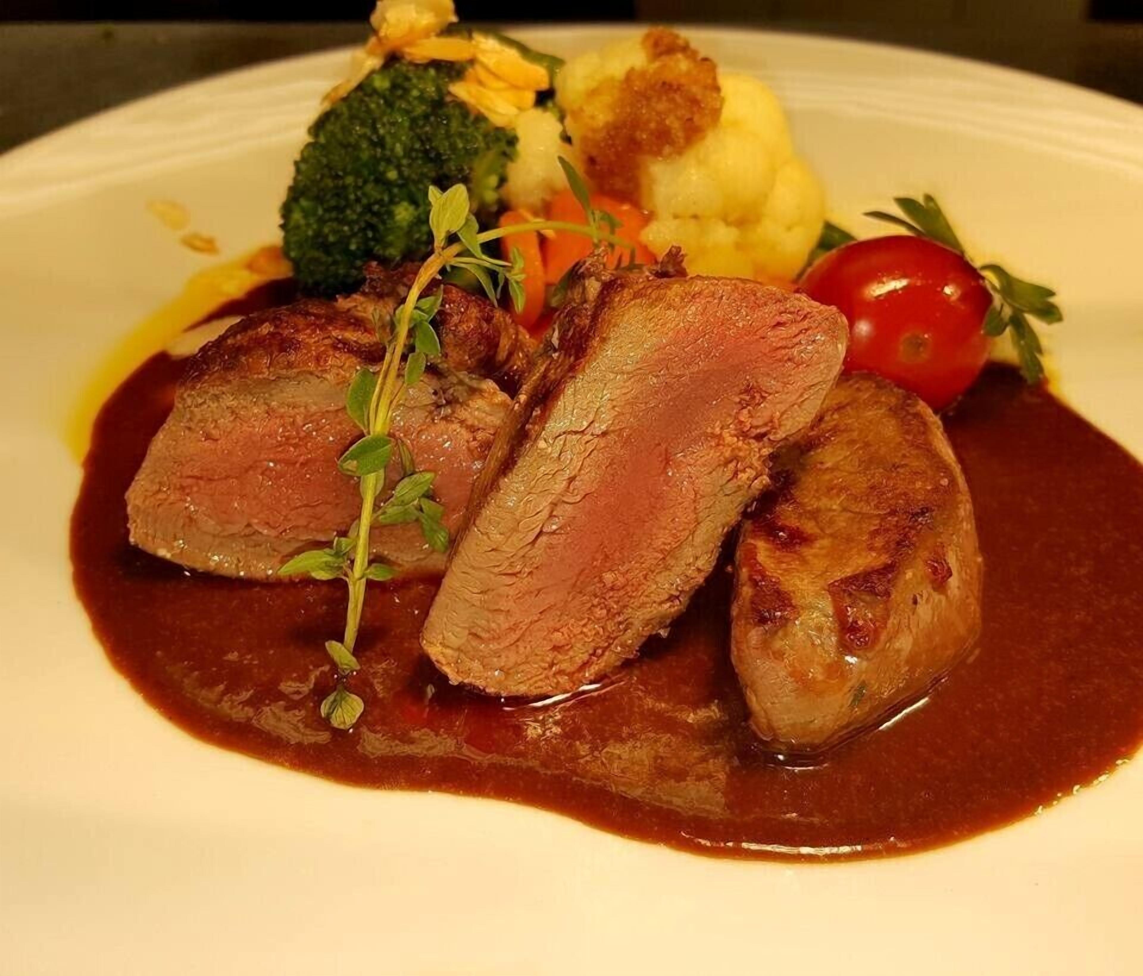 A plate with sliced meat, vegetables, and a sauce.