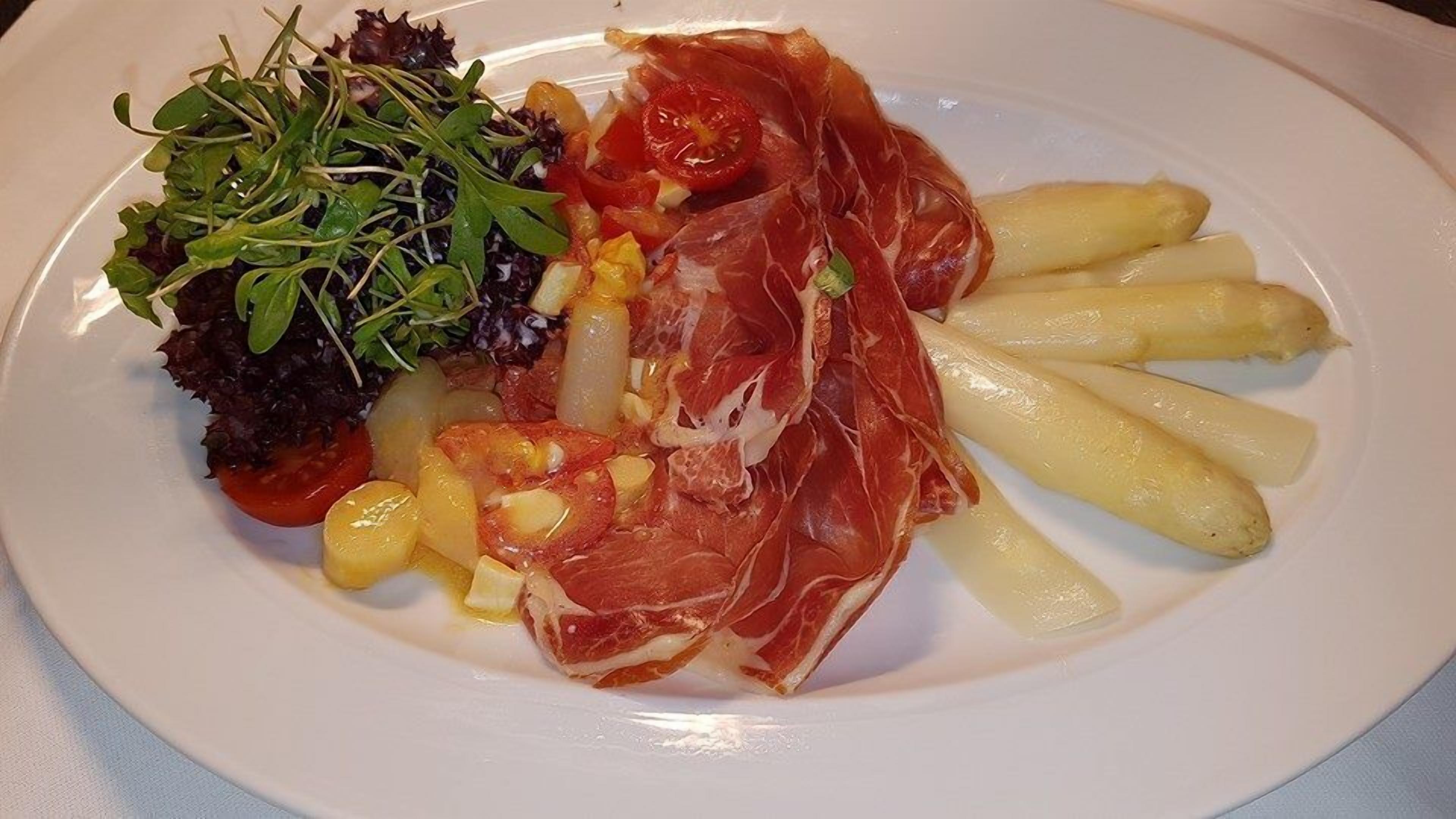 Un plato con jamón serrano, patatas hervidas, ensalada y maíz.