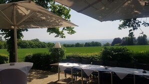 An outdoor dining area with tables and umbrellas, overlooking a green field and distant landscape. - Hotel Jägerhaus Esslingen (Esslingen)