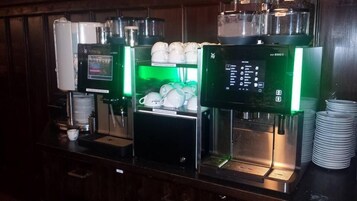 Una estación de café con varias máquinas expendedoras y una pila de vasos desechables.