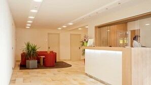 A reception area with a wooden reception desk, a red sofa, and a potted plant. - Hotel Jägerhaus Esslingen (Esslingen)