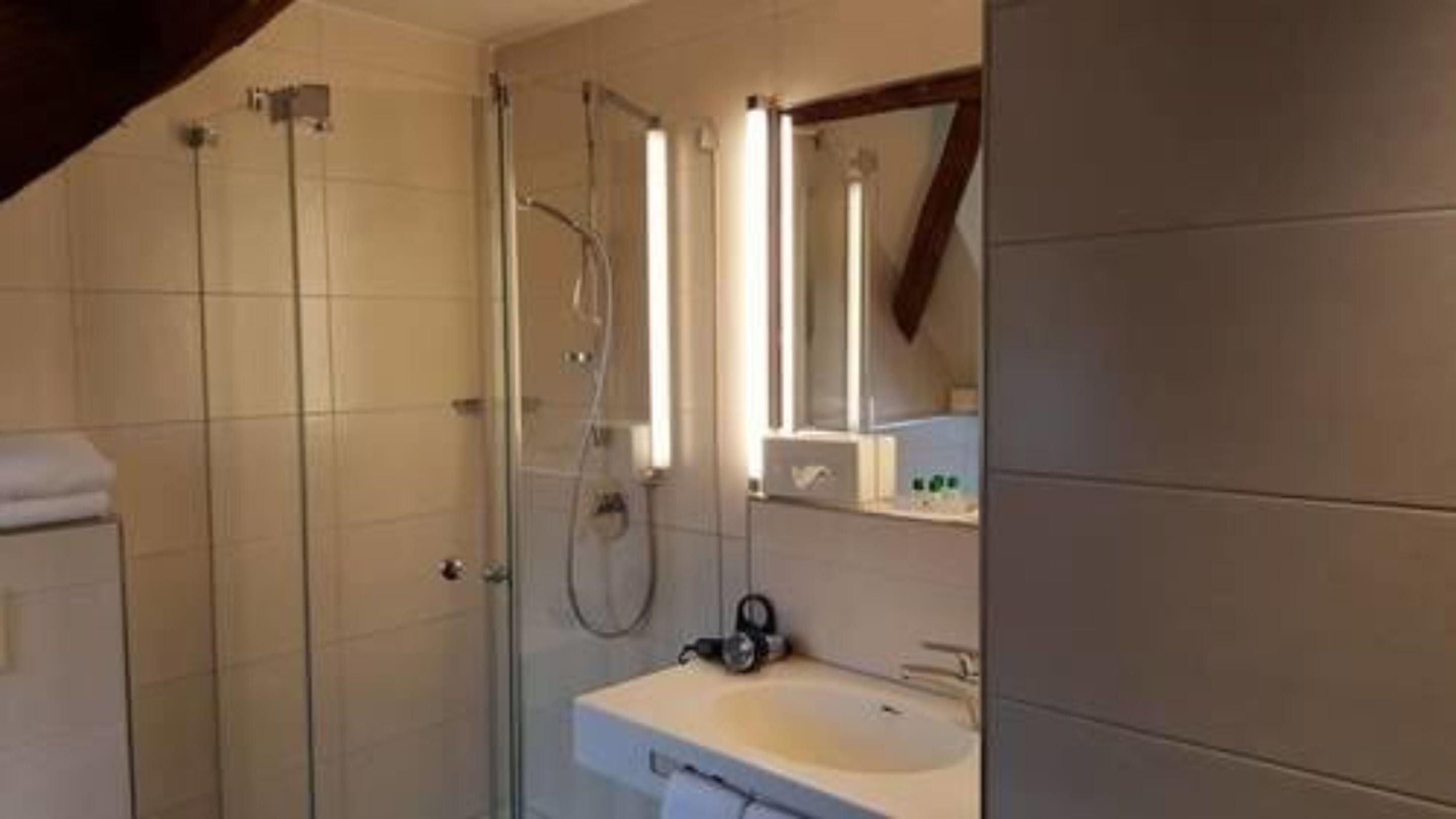 A modern bathroom with a glass shower enclosure, a white sink, and a mirror above it.
