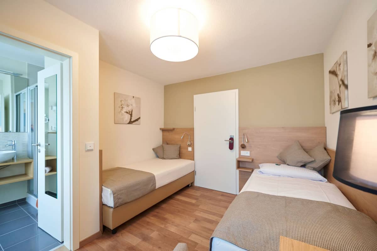 Une chambre d’hôtel avec un lit, un bureau et une télévision. Elle comprend une salle de bain avec un lavabo et une douche.