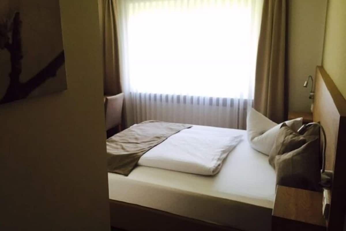 Une chambre d’hôtel avec un lit, une table de chevet, une lampe et une fenêtre avec des rideaux.