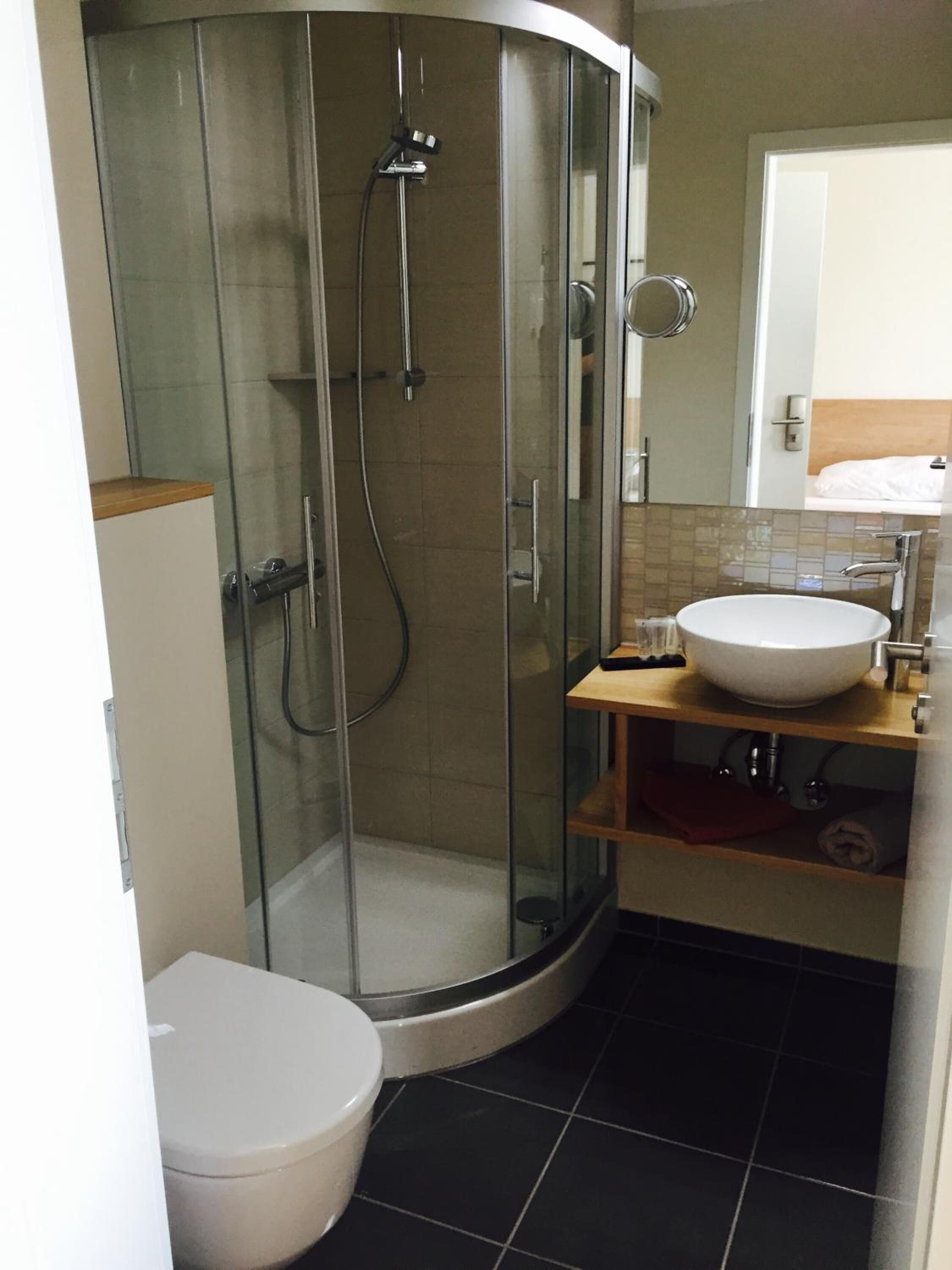 A modern bathroom with a glass-enclosed shower, a white toilet, and a sink with a wooden shelf.