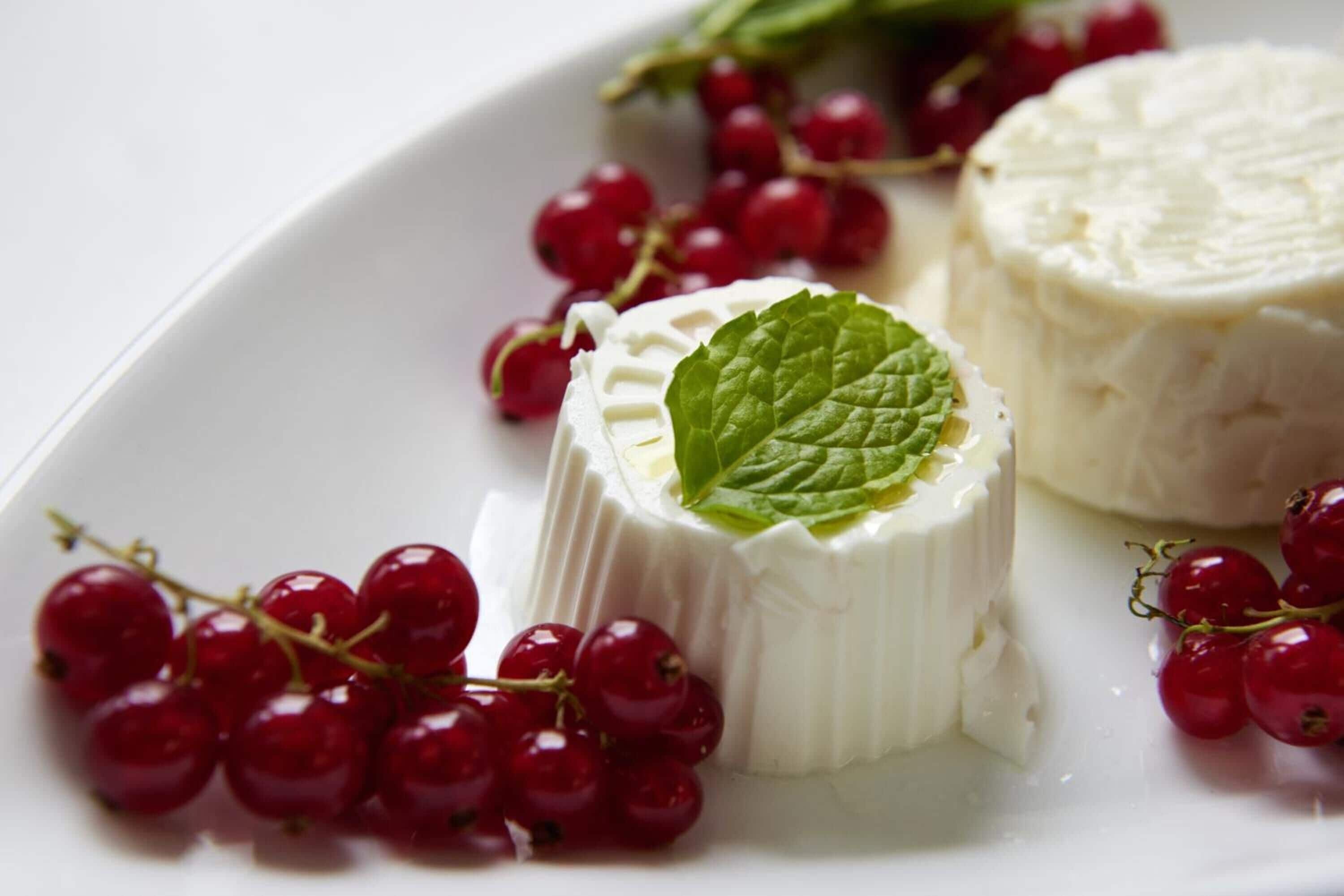 A white plate with a piece of white cheese and red currants.