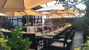 Un área de comedor al aire libre con mesas preparadas para el servicio, rodeada de sombrillas grandes y plantas en macetas.