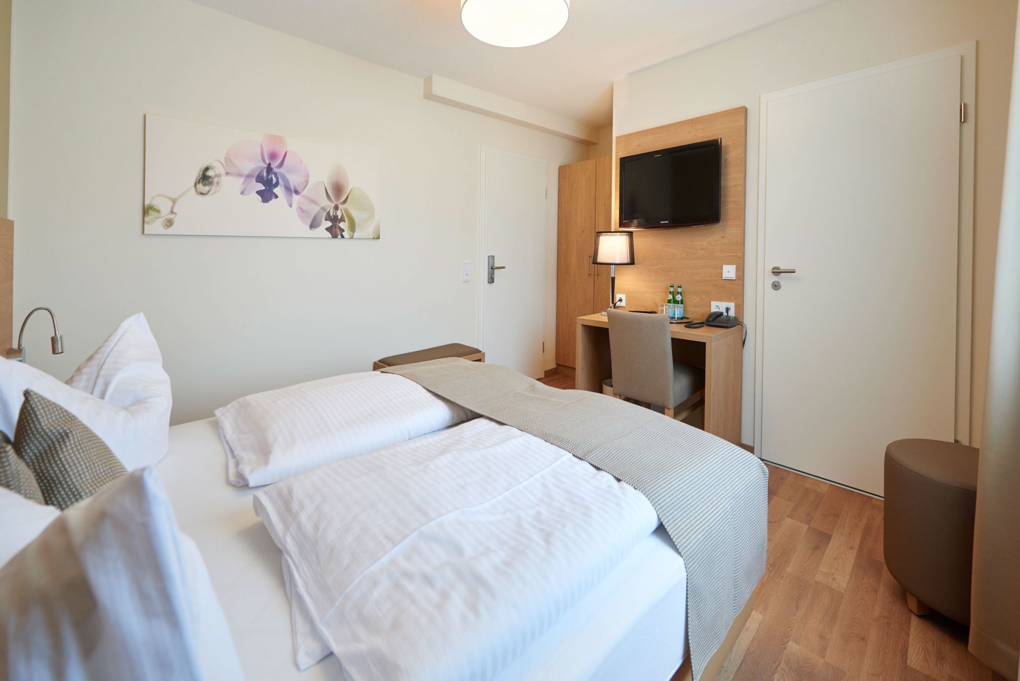 A hotel room with two beds, a desk, a TV, and a painting on the wall.