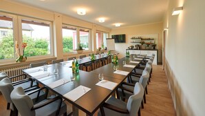Un salón de conferencias con una larga mesa, sillas y una zona de cocina al fondo.