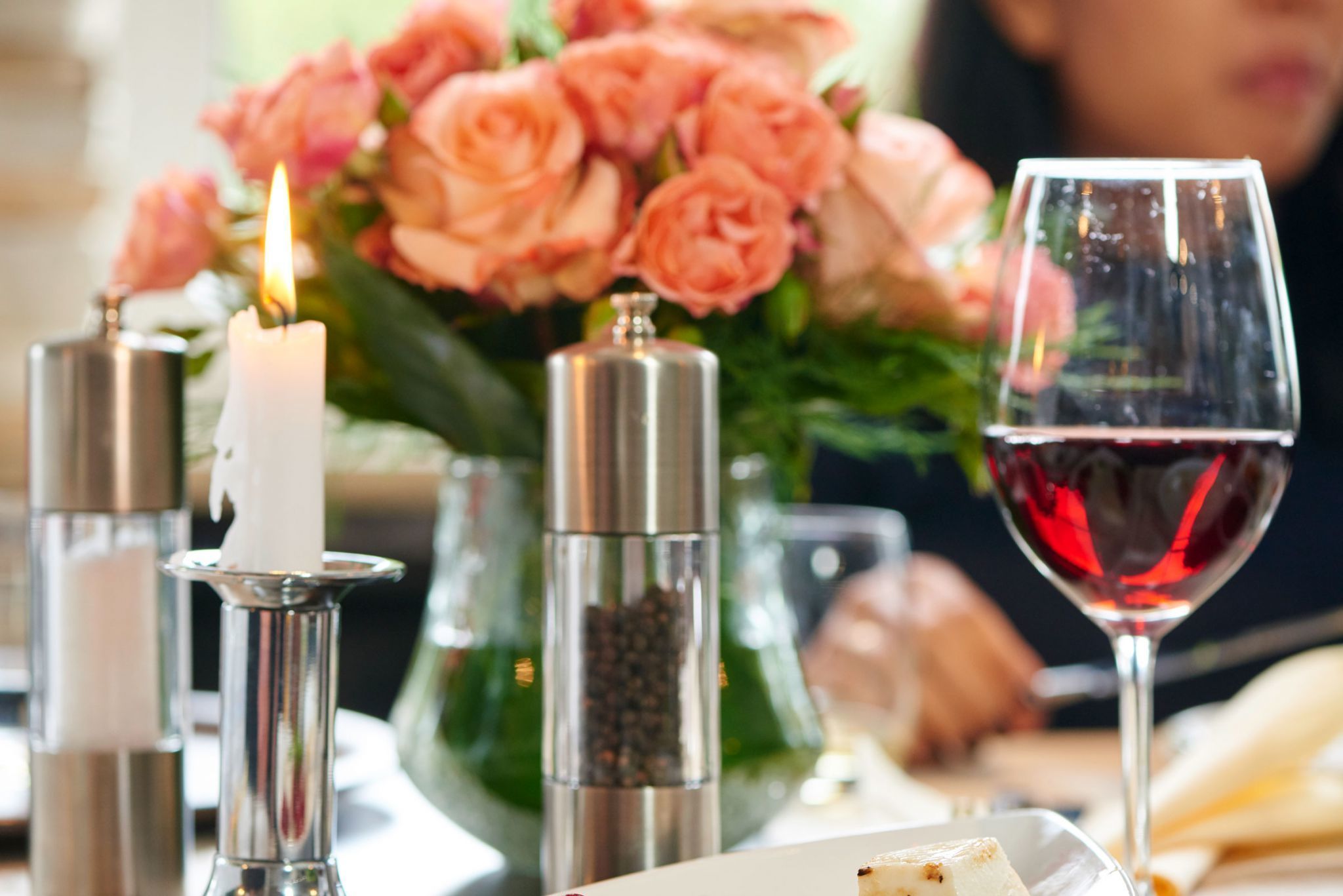 A table with a lit candle, a glass of red wine, and a bouquet of pink roses.