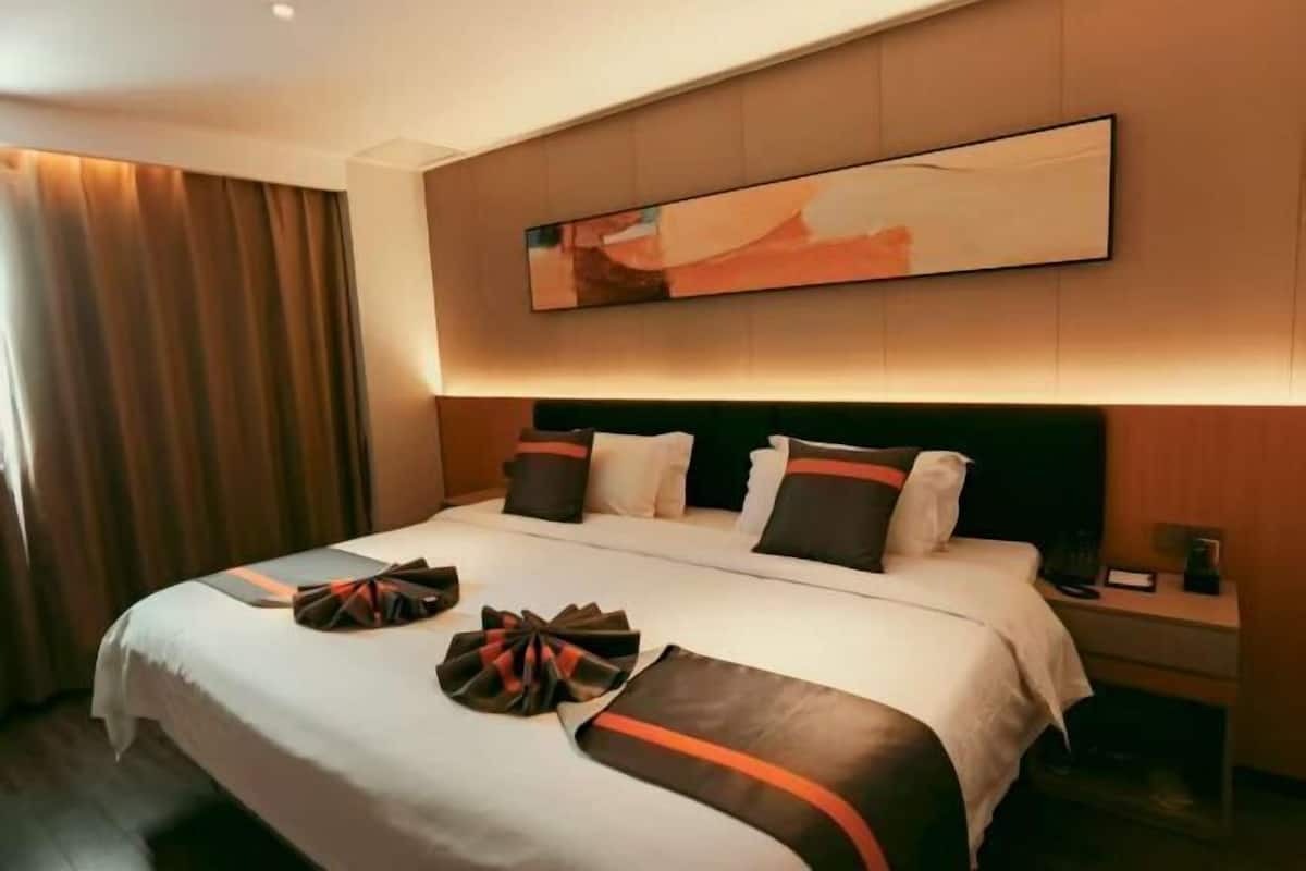 Habitación de hotel con una cama grande, cabecera, mesita de noche y una obra de arte colgada en la pared.