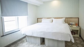A hotel room with a bed, bedside table, and a window with a blind. - Jinjiang Garden Hotel (Nantong)