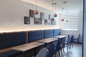 A restaurant with blue booths, tables, and chairs, with pendant lights and framed pictures on the wall.