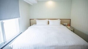 A hotel room with a large bed, a nightstand, a lamp, and a window. - Jinjiang Garden Hotel (Nantong)