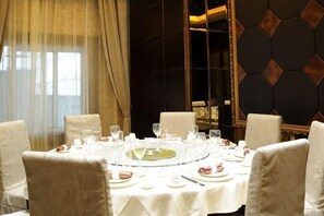 Mesa redonda para seis personas, con manteles y sillas blancas, en una habitación con pared de diseño oscuro y un espejo grande.