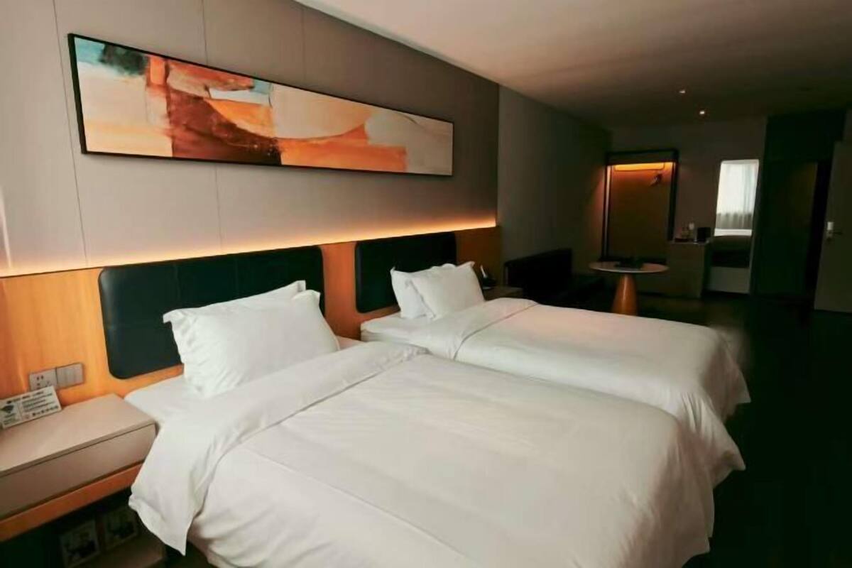 Une chambre d’hôtel avec deux lits, une table de chevet, une œuvre d’art accrochée au mur et une petite table avec une lampe.