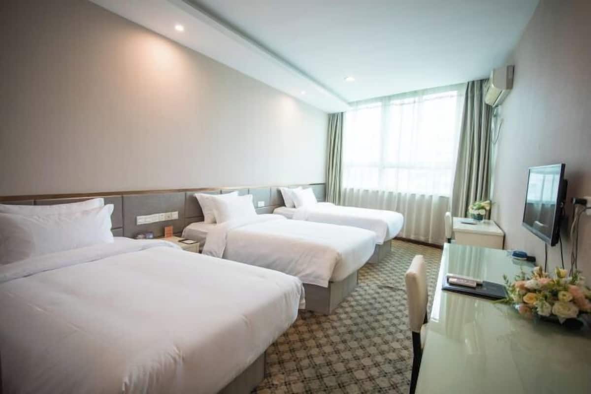 Habitación de hotel con tres camas, un escritorio con televisor y una ventana con cortinas.