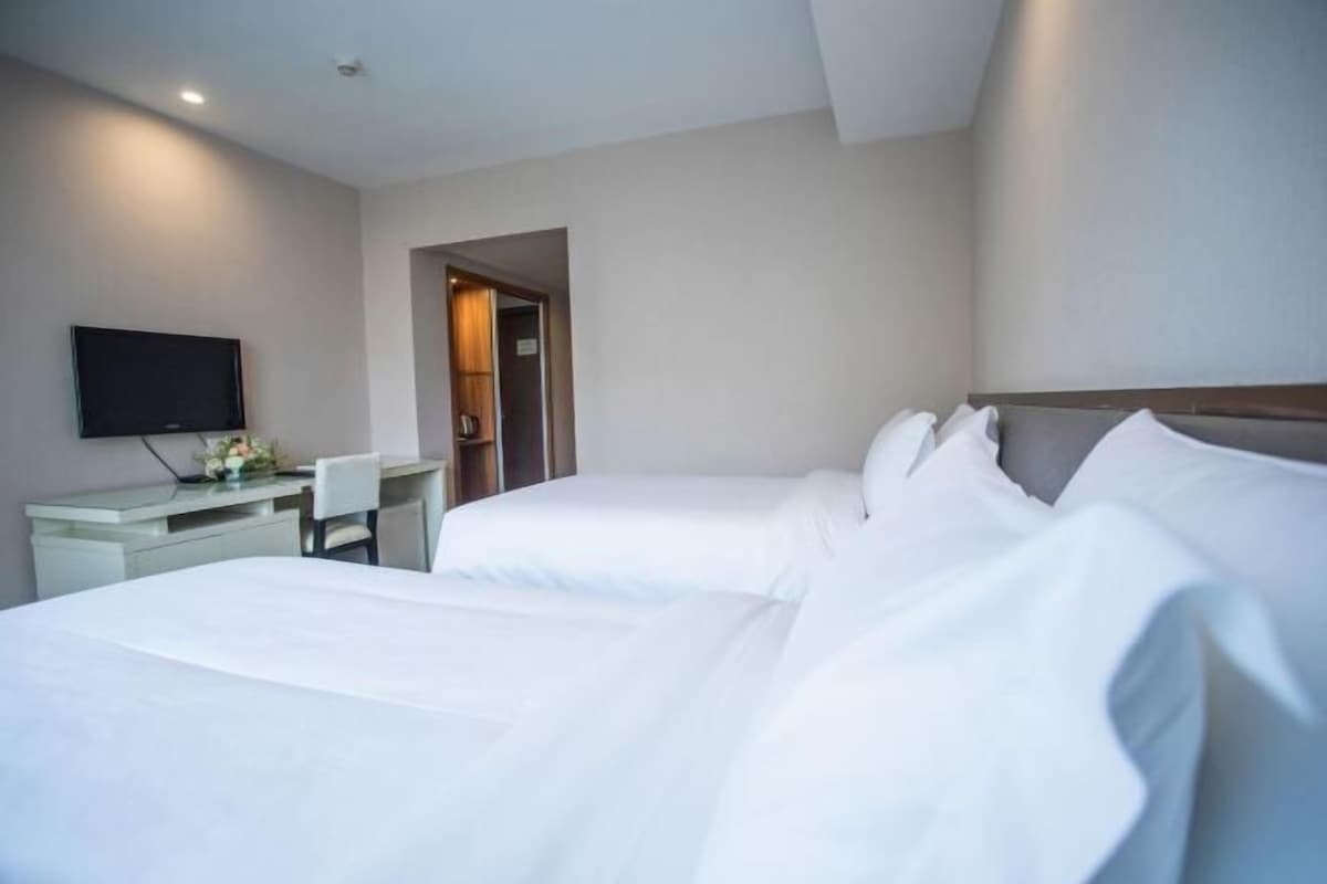 A hotel room with two beds, a desk, a chair, and a television.