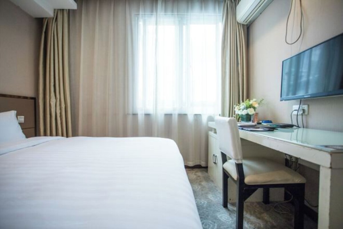 Hotellihuone, jossa on sänky, työpöytä tuolilla, televisio ja ikkuna, jossa on verhot.