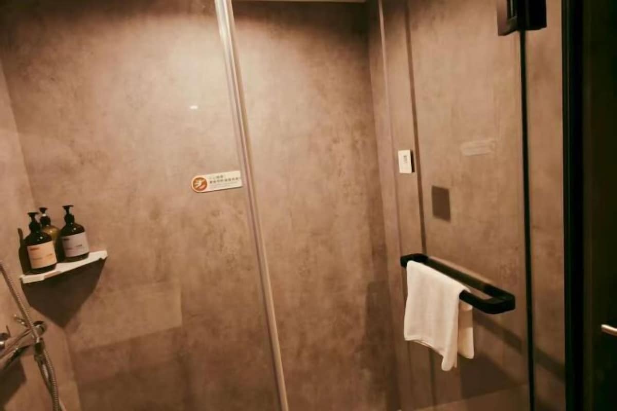 A bathroom with a glass shower enclosure, a towel rack, and toiletries on a shelf.