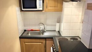 A compact kitchen with wooden cabinets, a stainless steel sink, a microwave, and a stove. - North Circular Studios 4 (Dublin)