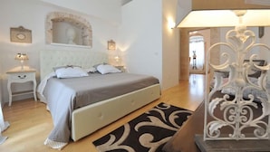 A bedroom with a large bed, a nightstand, a wall-mounted mirror, and a decorative lamp. - ArcoBello Suite Rooms (Castellana Grotte)