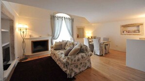 A living room with a fireplace, a sofa, a dining area with a table and chairs, and a mirror on the wall. - ArcoBello Suite Rooms (Castellana Grotte)