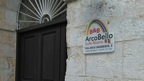 A dark wooden door with a stone wall and a sign for B&B ArcoBello Suite Rooms. - ArcoBello Suite Rooms (Castellana Grotte)