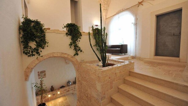 A stone staircase leading to a landing with a fireplace, surrounded by walls adorned with greenery. - ArcoBello Suite Rooms (Castellana Grotte)