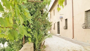 Un bâtiment avec un chemin de gravier, un portail en métal et un mur orné d’un emblème circulaire.