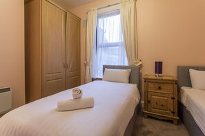 A bedroom with a bed, a nightstand, a wardrobe, and a window with curtains. - North Circular Studios 5 (Dublin)
