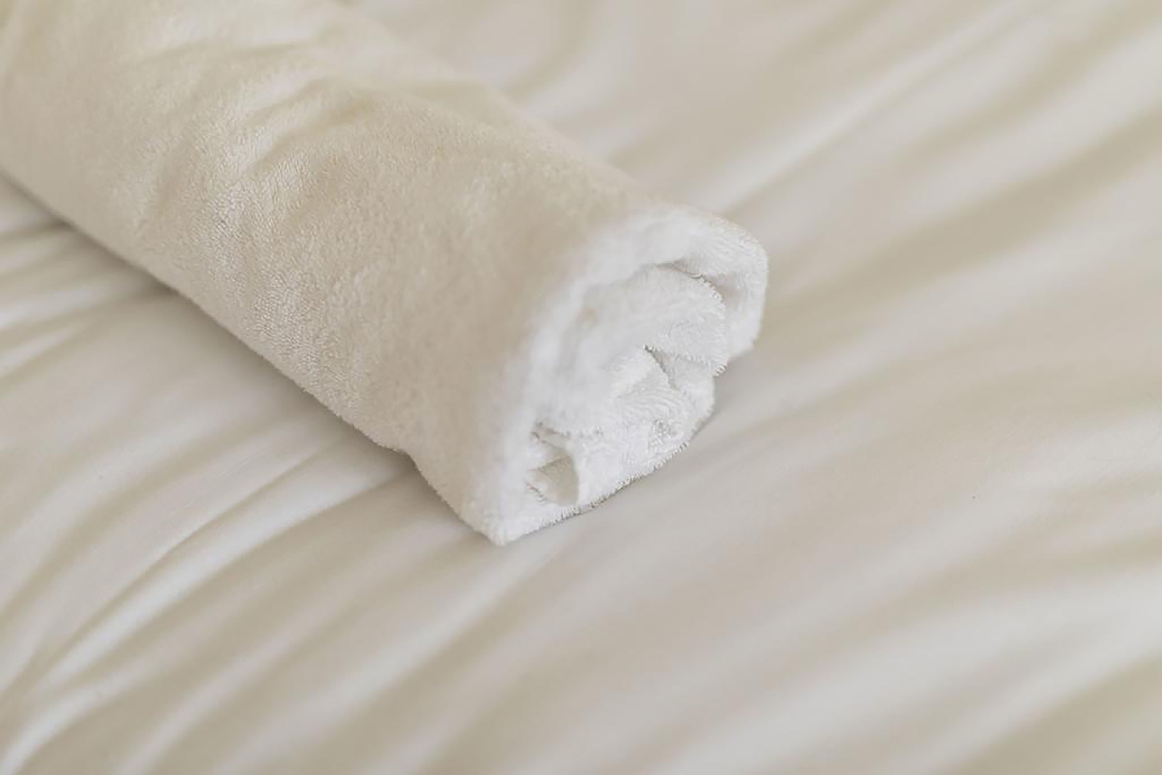 A neatly folded white towel on a bed with a textured surface.