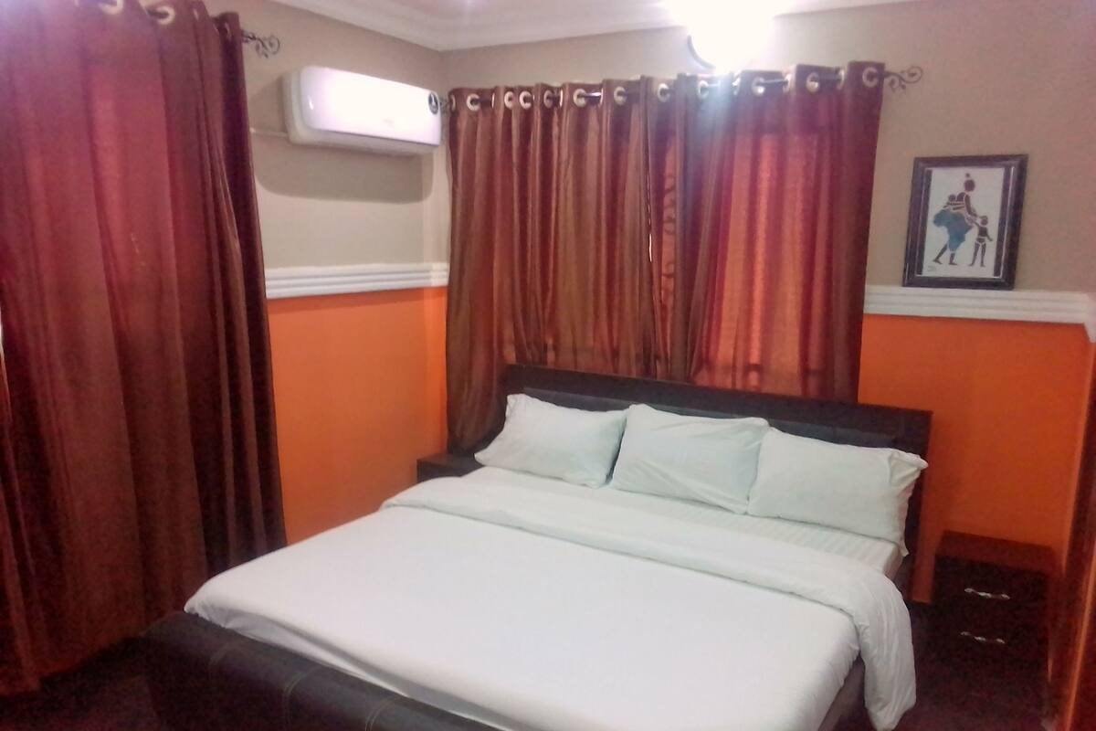 Quarto de hotel com cama, cortinas, aparelho de ar condicionado e um quadro na parede.