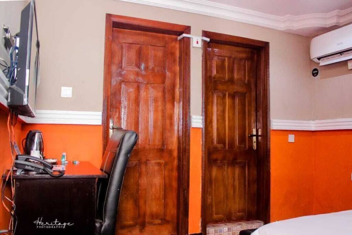 Quarto de hotel com duas portas de madeira, uma televisão, uma escrivaninha com cadeira e um aparelho de ar condicionado.
