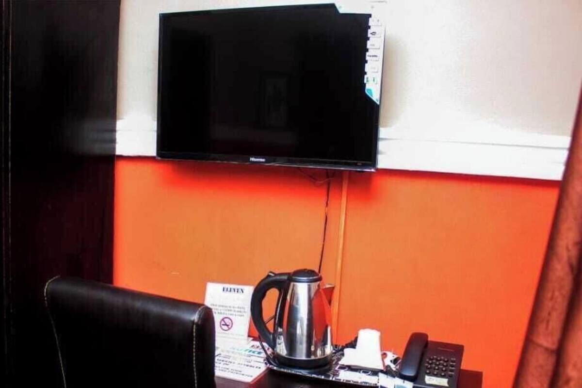 Quarto com televisão na parede, cafeteira sobre a mesa e telefone.