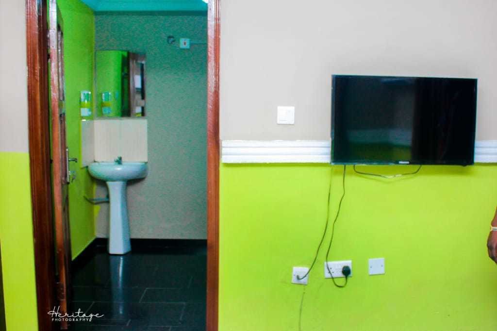 A bathroom with a green wall, a white sink, and a television mounted on the wall.