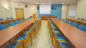 A conference room with long tables and chairs, a podium, a projector screen, and a clock on the wall.