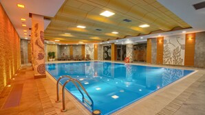 Una piscina interior con agua cristalina azul, rodeada de paredes con diseños florales y suelo de baldosas.
