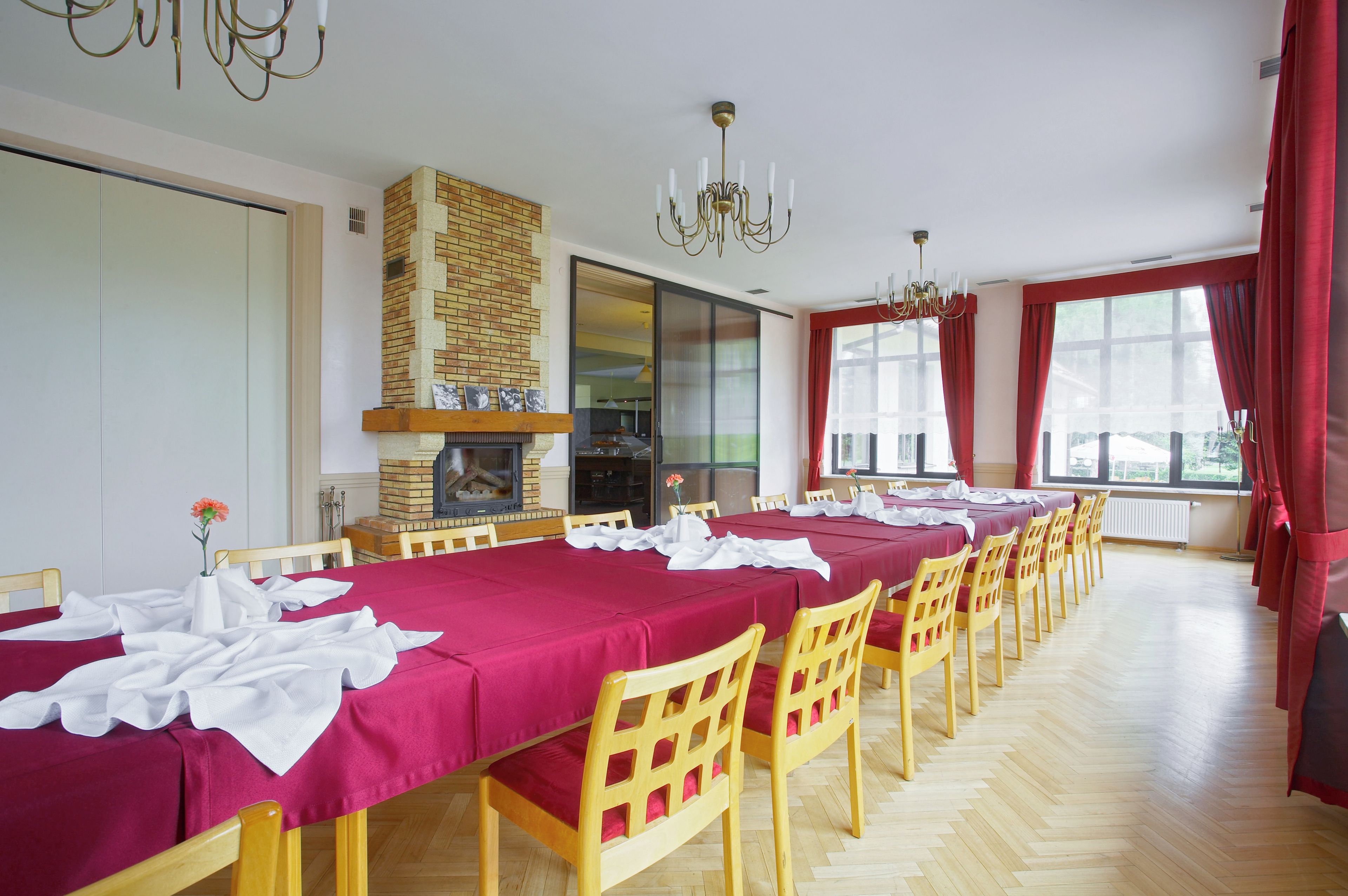 A dining area with multiple tables set for a meal, wooden chairs, a brick wall, and a chandelier.