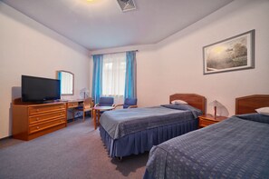 Quarto de hotel com duas camas, uma escrivaninha com televisão, uma cadeira e uma janela com cortinas.